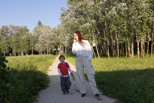 Mother and son enjoying a walk together on a sunny summer day, strolling along a path amidst lush green trees