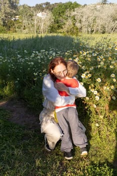 Mother and son share a tender moment in a field of daisies, enjoying the beauty of nature and the warmth of their bond