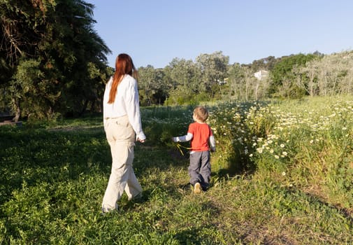 Mother and son enjoying a leisurely springtime walk amidst blooming daisies and lush greenery