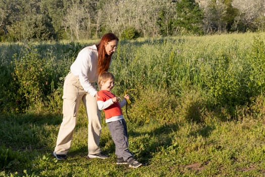 Happy mother and son having fun in a field, playing with wild plants on a sunny day