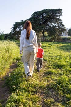 Mother and son enjoying a leisurely stroll through a vibrant green meadow on a sunny day