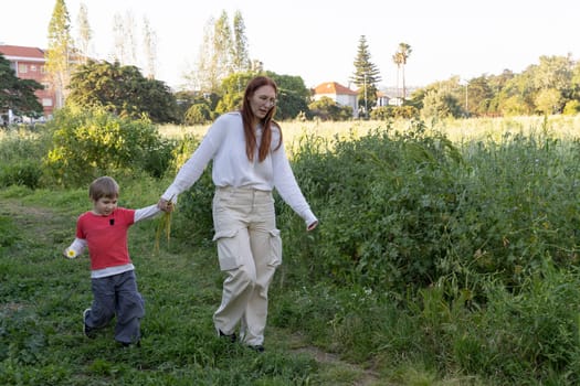 Mother and son enjoying a leisurely stroll through a field of tall grass, holding hands and creating a heartwarming moment