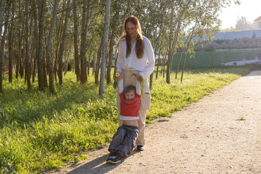 Happy mother swinging her son in a park, enjoying a sunny day surrounded by nature