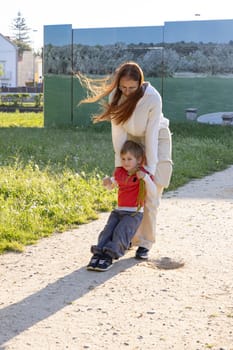 Mom pulling her son along a gravel path in a park on a summer day