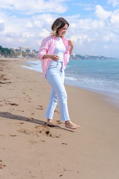 Happy young woman standing on the beach, looking at the camera with a smile. Dressed in casual clothes, she enjoys the sunny day and the relaxing ocean view in a peaceful coastal setting. Copy space