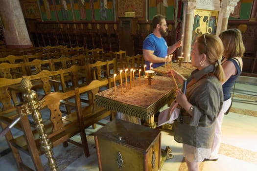 Rodas.Greece - june 05, 2025:  Individuals at the Church of Annunciation, lighting candles as part of a prayer and devotion ritual. A scene of faith in a historic temple.
