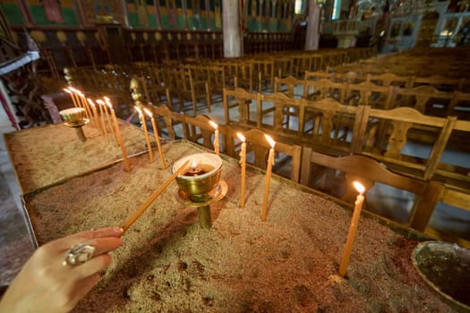 Focus on the act of lighting a votive candle, symbolizing faith and remembrance, inside the historic Church of Annunciation, with warm light illuminating the scene.
