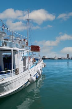A tour boat docked in the calm waters of Mandraki harbor, featuring St. Nicholas Fort and windmills. A sunny day in the Aegean.