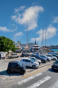 Rodas.Greece - june 05, 2025: View of a street with parked vehicles and the vibrant Rhodes port. The intersection of urban life and maritime activity.