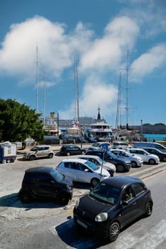 Rodas.Greece - june 05, 2025: View of a street with parked vehicles and the vibrant Rhodes port. The intersection of urban life and maritime activity.