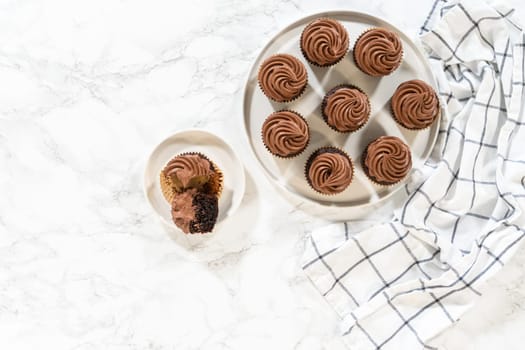 Flat lay. Freshly baked cupcakes have been masterfully infused with rich caramel and adorned with velvety chocolate frosting, all elegantly presented on a pristine white serving plate.