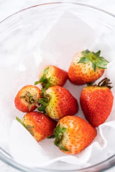 Freshly washed and dried strawberries are carefully arranged in a glass bowl lined with paper towel, ready for snacking or further use.