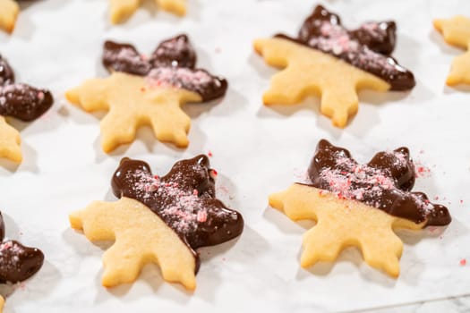 Close-up of a chocolate-dipped snowflake sugar cookie topped with crushed peppermint candy on parchment paper.