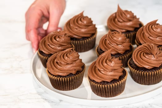 Freshly baked cupcakes have been masterfully infused with rich caramel and adorned with velvety chocolate frosting, all elegantly presented on a pristine white serving plate.
