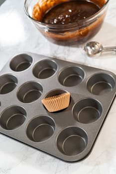 Getting ready to bake delicious chocolate cupcakes, we carefully line the cupcake pan with paper liners, ensuring a delightful treat awaits.