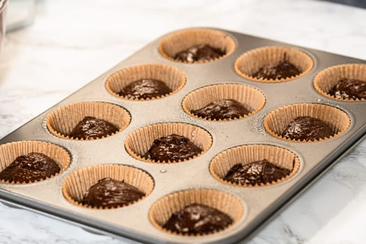 The process involves carefully scooping the rich batter into the waiting cupcake pan.