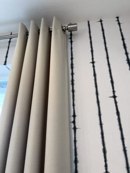 Neutral-colored curtain hanging on a silver rod, set against a bold modern wallpaper with vertical black lines. Great for window treatment product images or home decor features.