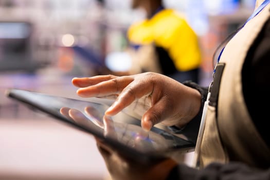 Smart factory engineer using a tablet to develop production line layouts in CAD software. Close up of african american worker optimizing industrial floor configurations with digital tool.