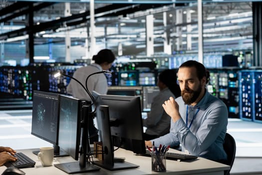 Technician using PC in data center to update server tech, configuring equipment using software tools. Server room employee reviewing hardware analytics, ensuring reliable network operations