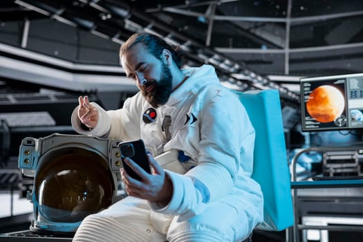 Cosmonaut doing videocall with family using smartphone during Mars expedition. Astronaut in remote call with loved ones using mobile phone in spaceship, exploring red planet