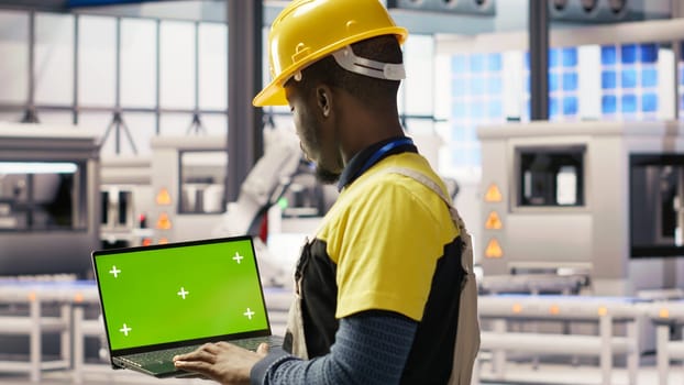 Engineer in smart factory using green screen laptop to analyze IoT sensors data. Industry 4.0 plant expert performing system diagnostics on chroma key mockup notebook to reduce downtime, camera B