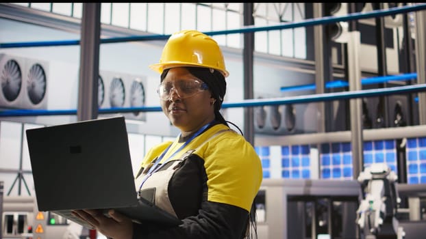 Woman working in industry 4.0 plant using notebook, following maintenance procedures. Smart factory staff member analyzing data on laptop to predict gear failures, camera A