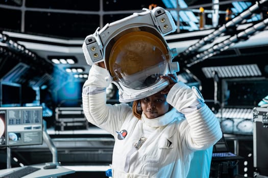 Portrait of female cosmonaut putting on cosmic gear helmet, preparing for planetary mission outside. African american woman in orbital station beginning landing procedures on solar system planet