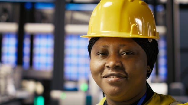 Happy engineer in smart photovoltaics factory looking at system performance metrics. Smiling worker in solar panels plant tracking energy production through IoT sensors, camera B close up