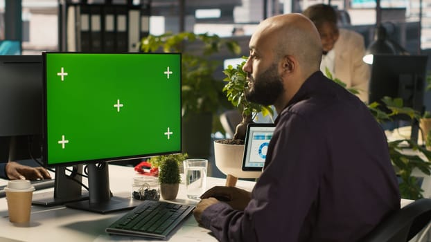 Employee at work using isolated screen PC to check progress done on customer commissioned project. Office clerk in front of mockup computer reading data statistics on paperwork after audit, camera A