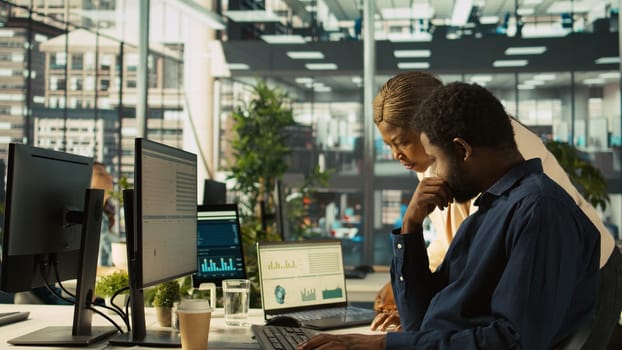 Employee in office showing revenue figures on laptop to manager. Accountant presenting company statistical numbers on notebook to supervisor after finishing job tasks, camera B