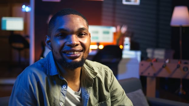Portrait of african american person smiling and working in his living room, using laptop to solve remote freelancing tasks as a self employed guy. Young adult feels relaxed at home. Camera A.