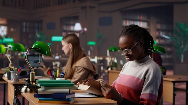 Black girl reading books and handwritten class notes right before the exam, making preparations all night to get a high grade for scholarship. Young adult shows dedication and ambition. Camera A.