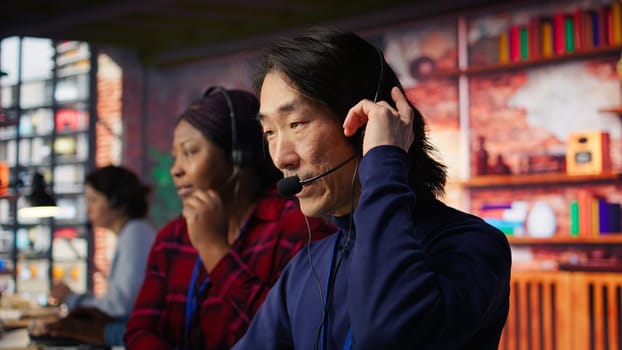 Customer center employee gesturing loud Asian senior agent to quiet down while working African american woman working in call center worker upset by noises in office made by colleague, camera B