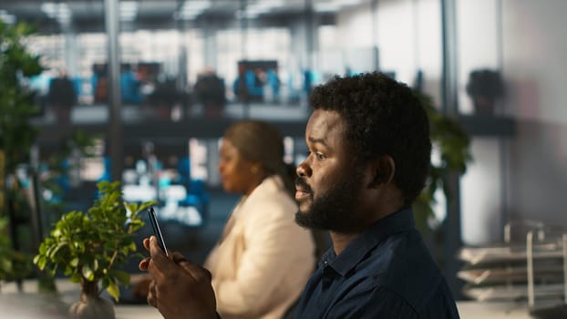 Employee in office taking break from checking documents to text friends using smartphone, relaxing. Accountant in office pausing tasks to answer messages on mobile phone, camera A