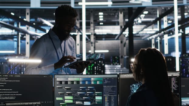 Server hub manager talking with programmer using node tree software to optimize system health. Data center supervisor overseeing IT expert analyzing equipment issues using AI visualization, camera B