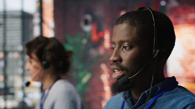 Diverse customer center workers assisting clients with installing software. Multiethnic team of call center agents using remote access tools to connect to customer devices, fixing errors, camera A