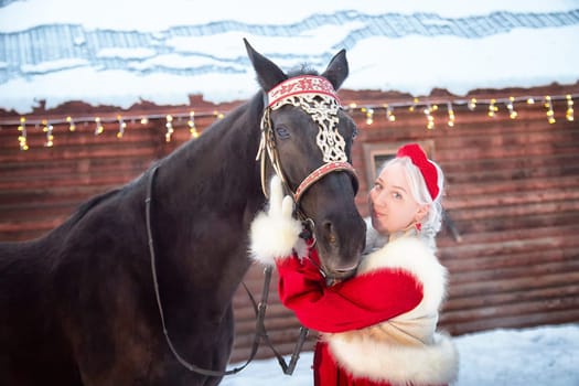 A stunning Russian girl dressed in traditional attire enjoys a winter photo shoot with a horse during Maslenitsa.