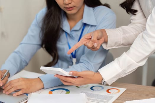 Two women engage in a focused discussion, reviewing financial information on a tablet in a modern office setting.