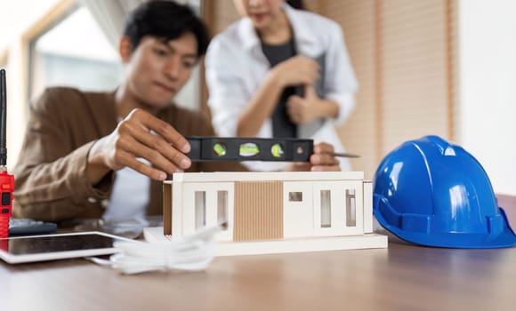 Two architects discussing a miniature building model, focusing on sustainable design principles and ESG values in construction.