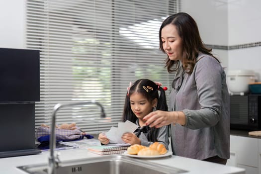 A mother and daughter share a joyful moment in the kitchen, engaging in learning activities with notes and pastries.