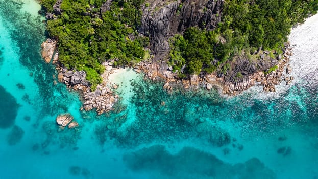 Large granite boulders meet vibrant turquoise waters, with a small, secluded sandy beach nestled among lush greenery. Curieuse, Seychelles.