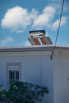 A solar water heater installed on the rooftop of a building demonstrating the commitment to renewable energy. Blue sky with scattered clouds.