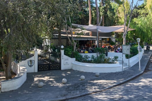 Rodas.Greece - june 06, 2025: A picturesque outdoor cafe terrace in Rhodes, Greece, surrounded by trees and greenery, with people enjoying the ambiance, ideal for leisure.