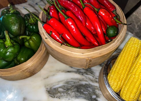 Vibrant red chili peppers and fresh green bell peppers arranged in bamboo bowls creating a colorful display perfect for food themes, cooking, healthy eating, and agricultural or culinary content.
