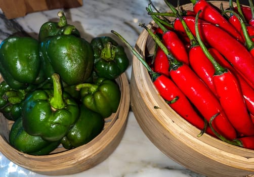 Vibrant red chili peppers and fresh green bell peppers arranged in bamboo bowls creating a colorful display perfect for food themes, cooking, healthy eating, and agricultural or culinary content.