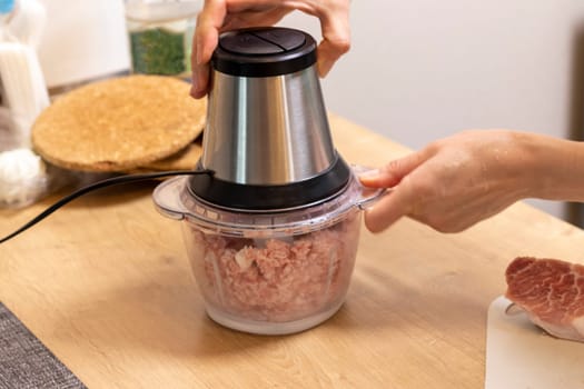 Woman mince the meat in the electrical chopper on the kitchen counter top