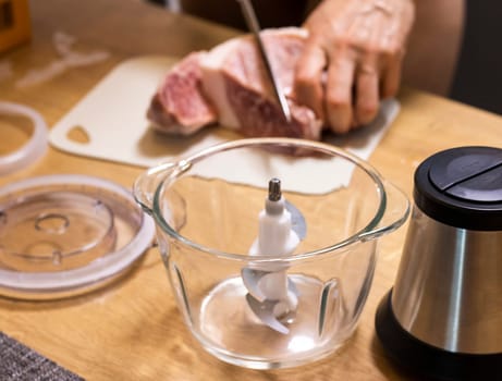 Woman cuts the meat, prepares it to grind it in electrical chopper