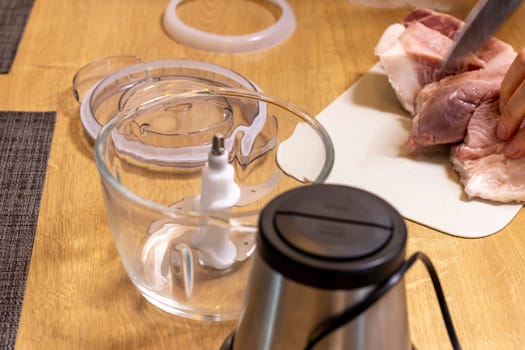 Woman cuts the meat, prepares it to grind it in electrical chopper