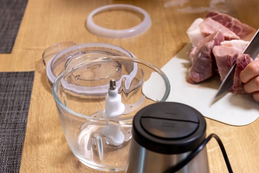 Woman cuts the meat, prepares it to grind it in electrical chopper
