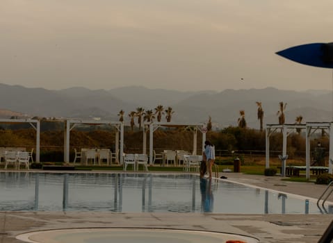 A young man and woman share a warm embrace beside a tranquil swimming pool in Cyprus, surrounded by serene holiday vibes.